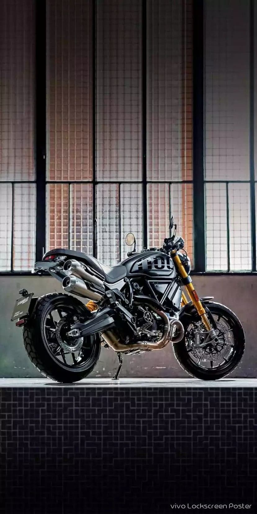 Ducati Scrambler motorcycle with gold forks and dual exhaust pipes positioned before industrial gridded windows.