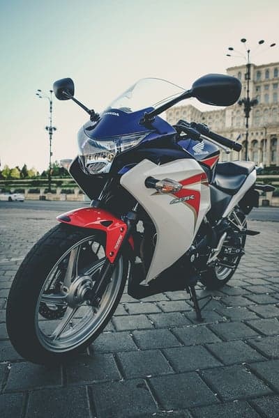 Red, white, and blue Honda CBR motorcycle parked on cobblestones