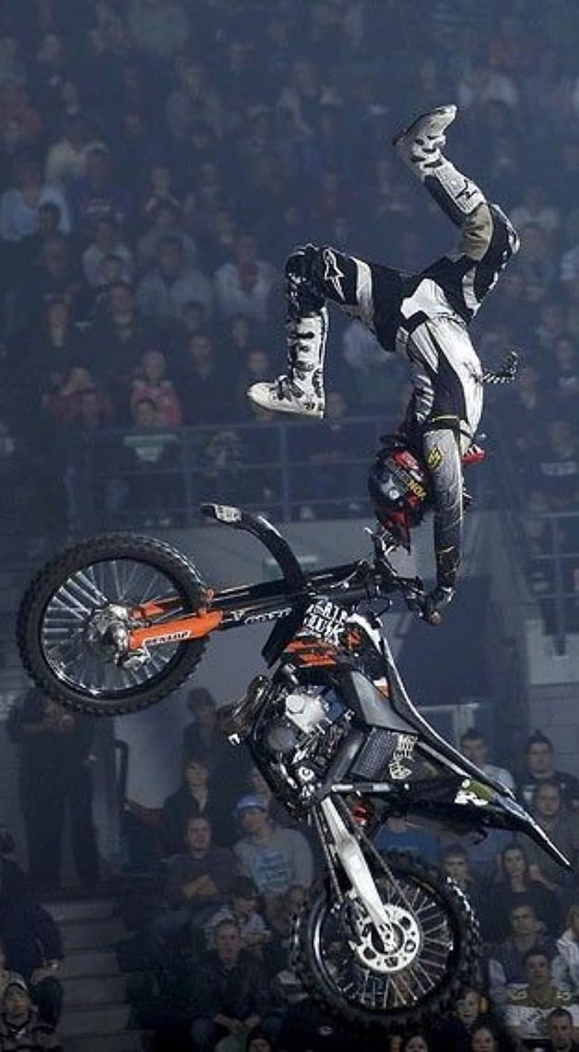 Motocross rider hangs upside down from a bike in mid-air while performing a stunt above a blurred crowd.