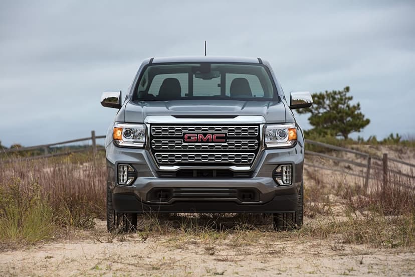 Metallic grey GMC pickup truck facing forward on a sandy coastal dune with tall grass and a cloudy sky.