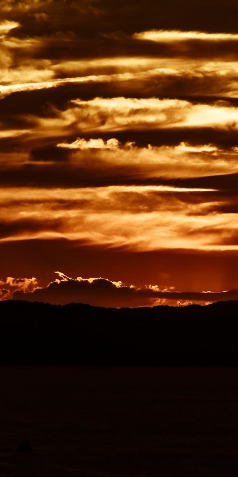 Textured orange clouds illuminated by golden light from below against a dark, low-lying land silhouette.