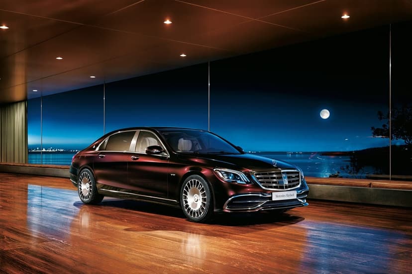 Mercedes-Maybach S-Class parked in a glass-walled room overlooking a moonlit ocean at night with warm lighting.