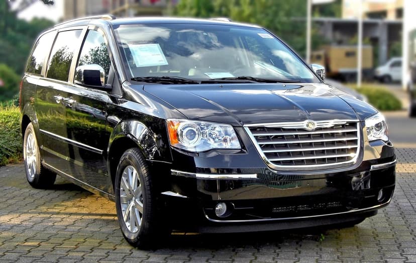 Front view of a black Chrysler minivan parked on textured gray bricks with a blurred green background.