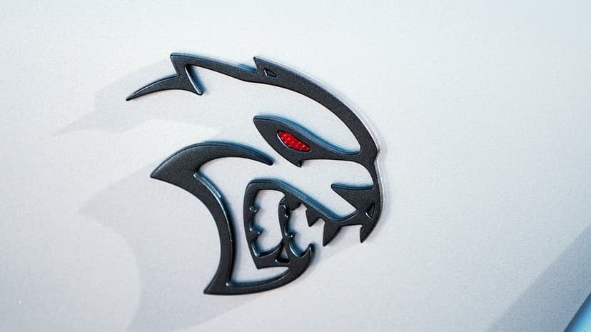 Dark Dodge Hellcat badge with a glowing red eye mounted on a silver metallic car panel with subtle reflections.
