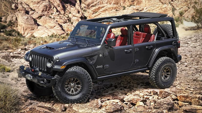 Black Jeep Wrangler 392 with red seats and off-road tires parked on rocky desert terrain under bright sunlight.