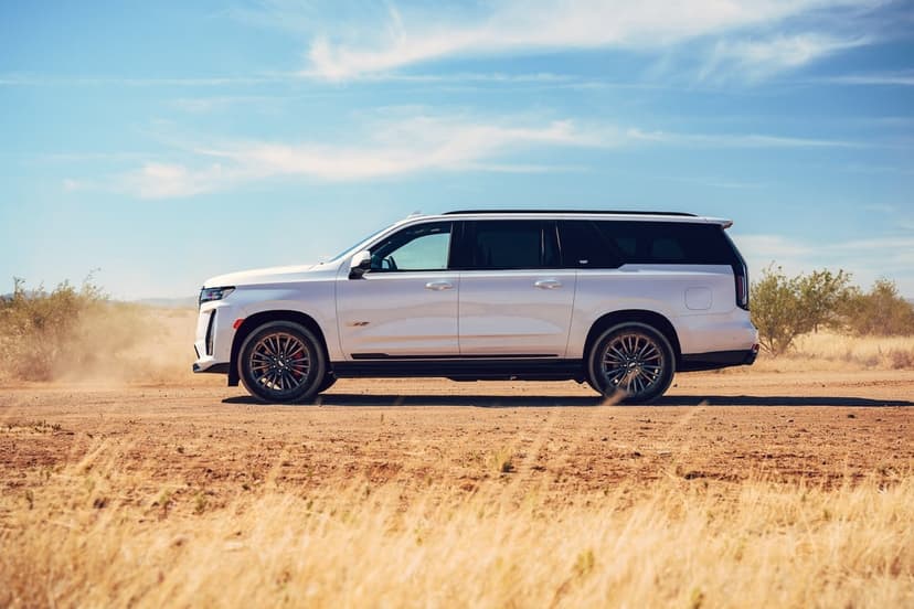 Side profile of a white Cadillac Escalade-V on a dusty dirt road under a clear blue sky with golden grass.