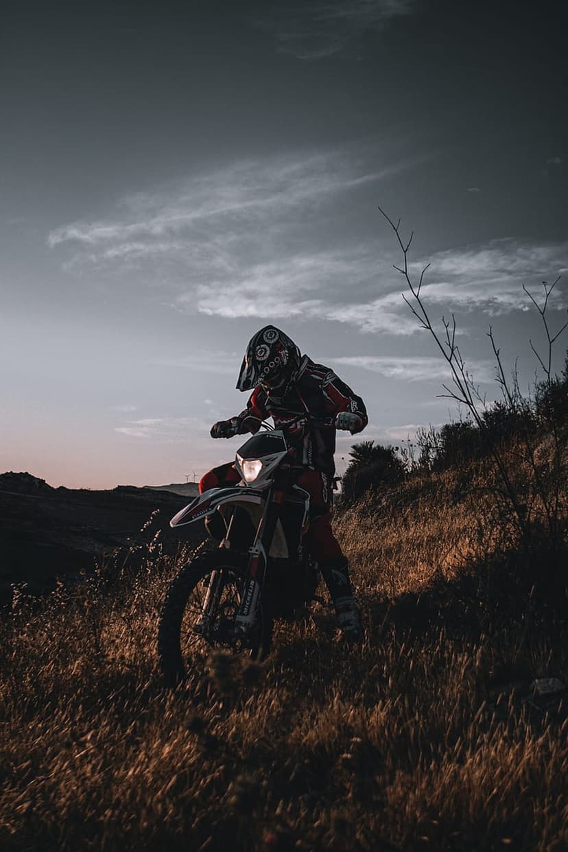 Dirt bike rider navigates a grassy hill at sunset with a patterned helmet and glowing golden light.