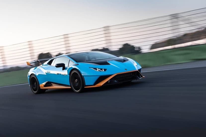 Blue and orange Lamborghini Huracan STO speeding on a racetrack with motion blur and soft morning lighting.