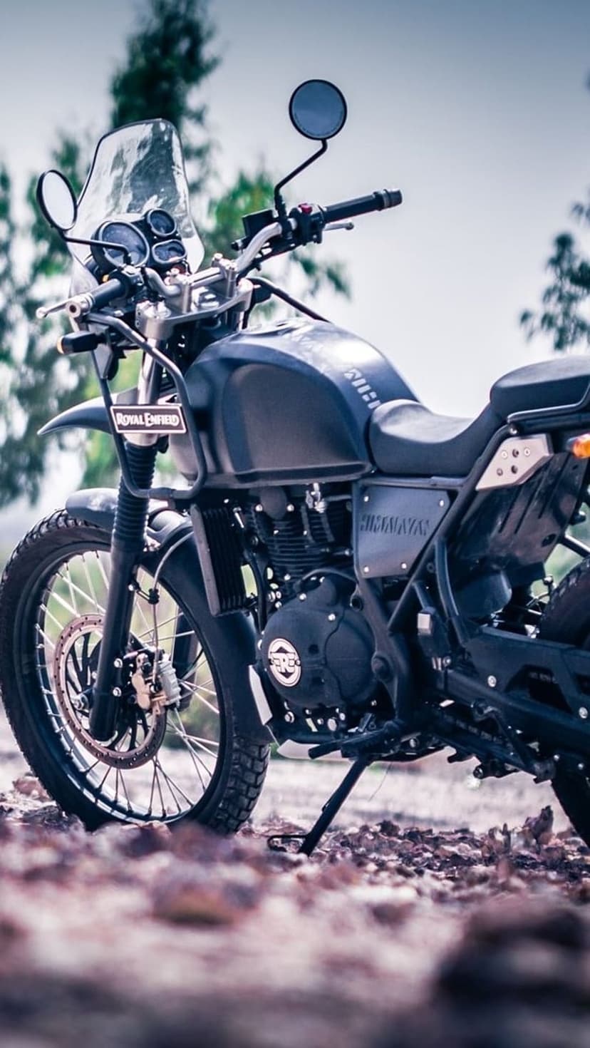 Royal Enfield Himalayan motorcycle on a rocky path featuring engine details, front wheel, and blurred trees.