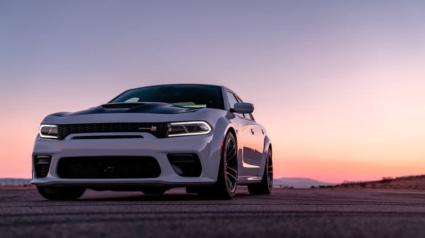 White Dodge Charger Scat Pack Widebody at sunset on a desert road with a purple and orange sky.