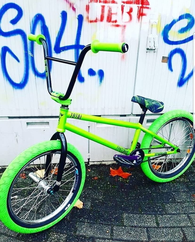 Neon green BMX bike with matching tires parked against a white wall decorated with blue and red graffiti tags.