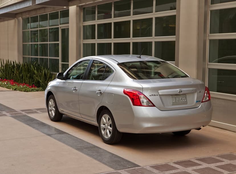Silver Nissan Versa SL sedan parked on a paved driveway in front of a building with large glass windows.