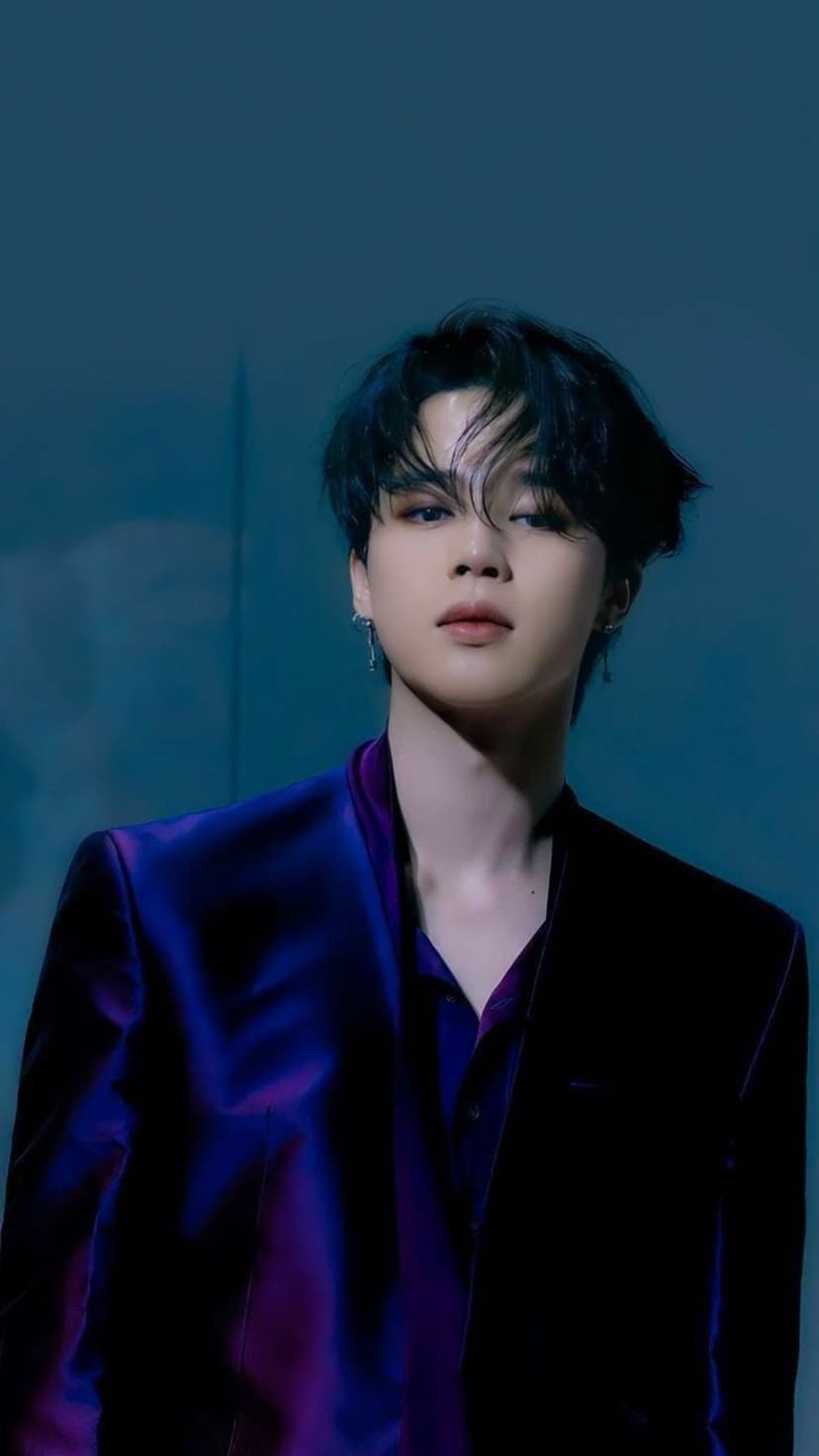 Jimin from BTS wears a purple blazer and shirt against a dark blue background with dramatic side lighting.