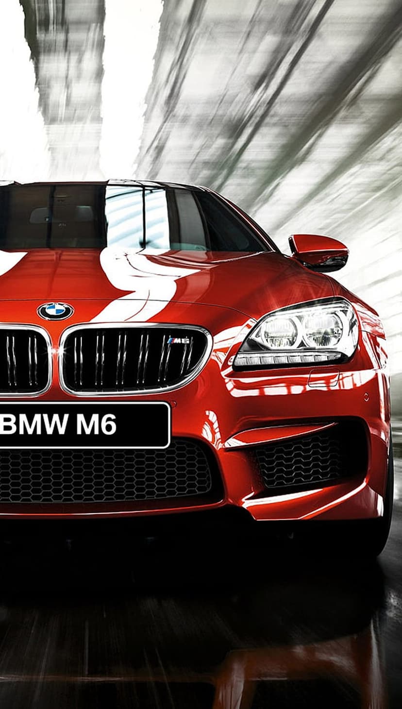 BMW M6 in red with white racing stripes and glowing headlights captured from a low angle with motion blur.