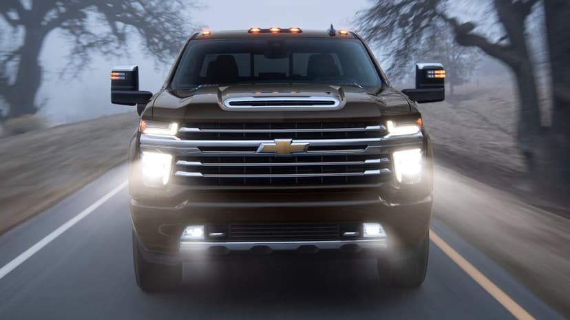 Front view of a dark brown Chevrolet Silverado truck on a misty road with glowing LED headlights and chrome grille.