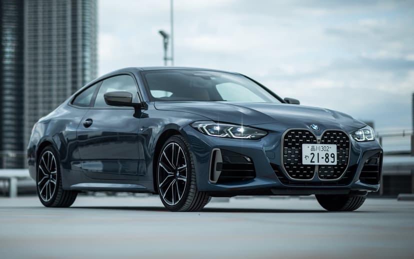 Dark blue BMW coupe parked on a rooftop with glowing LED headlights and a blurred city skyline background.