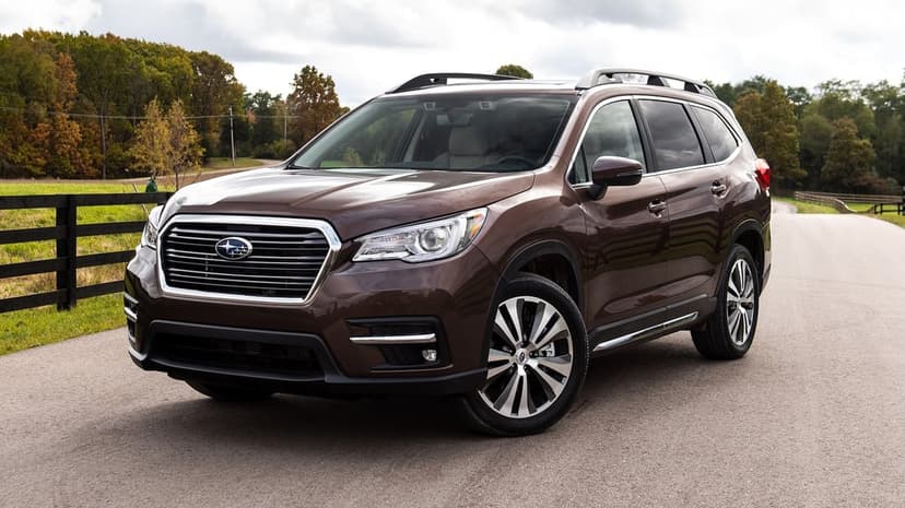 Brown Subaru Ascent SUV parked on a paved road with a black fence and autumn trees in the background.