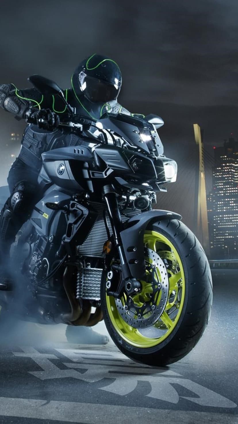 Motorcyclist in neon green gear on a sportbike with glowing wheels against a blurred night cityscape background.