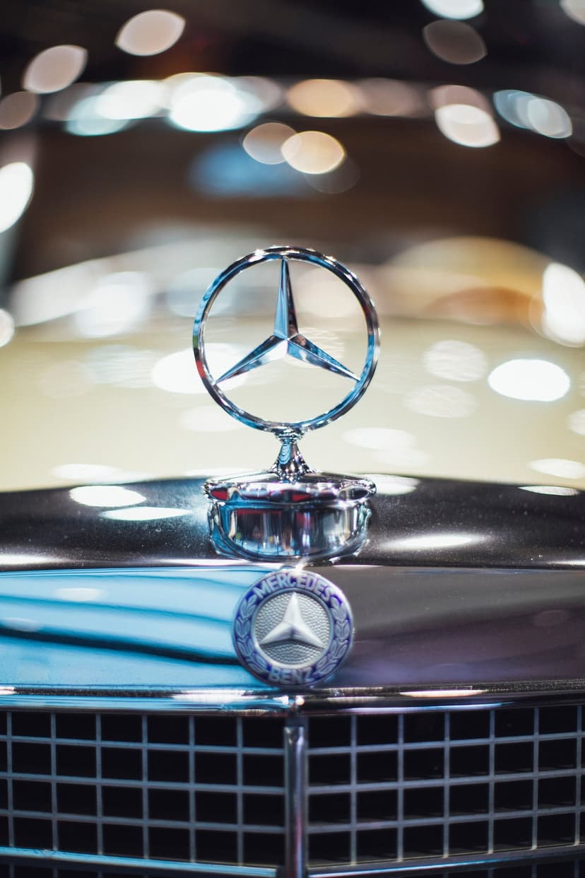 Mercedes-Benz three-pointed star hood ornament stands atop a chrome grille with blurred light reflections.