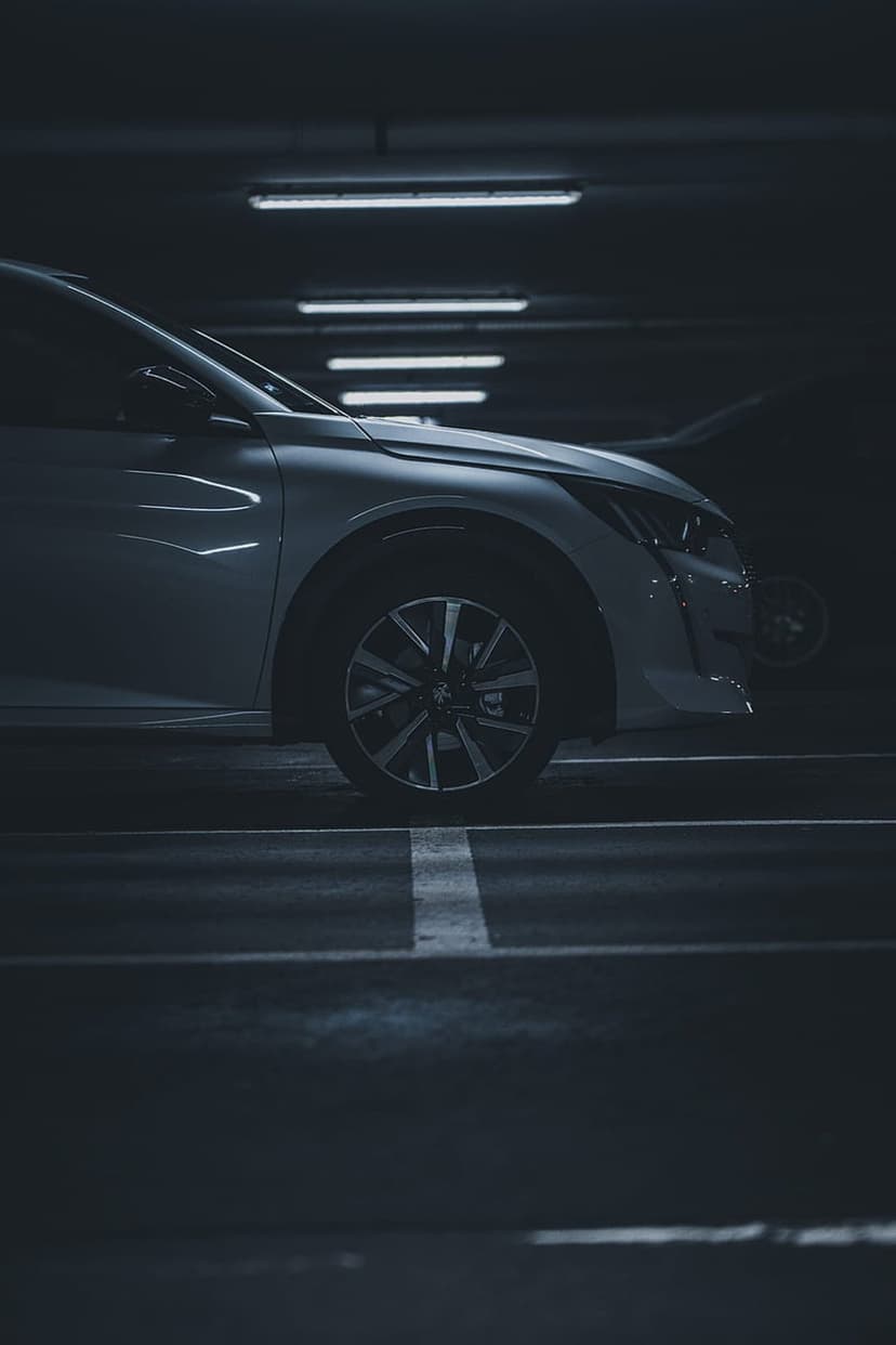 Modern car front wheel and fender illuminated by overhead fluorescent lights in a dark, shadowy parking garage.