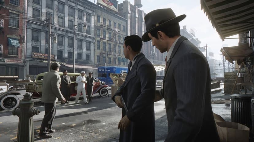 Two men in suits stand on a 1930s city street with vintage cars and old brick buildings in the background.