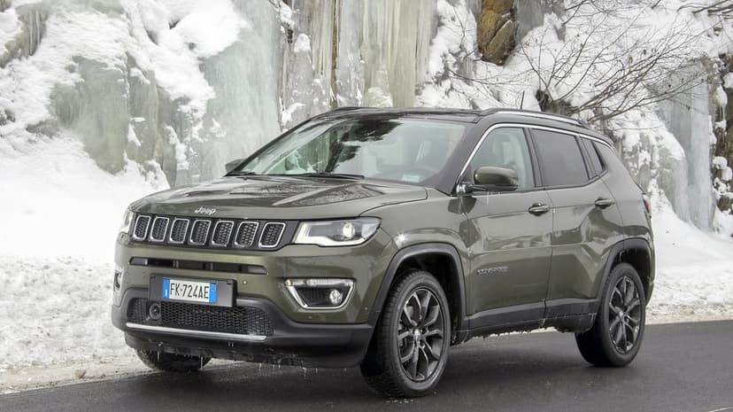 Olive green Jeep Compass SUV parked on a dark road in front of a massive frozen waterfall and snow.
