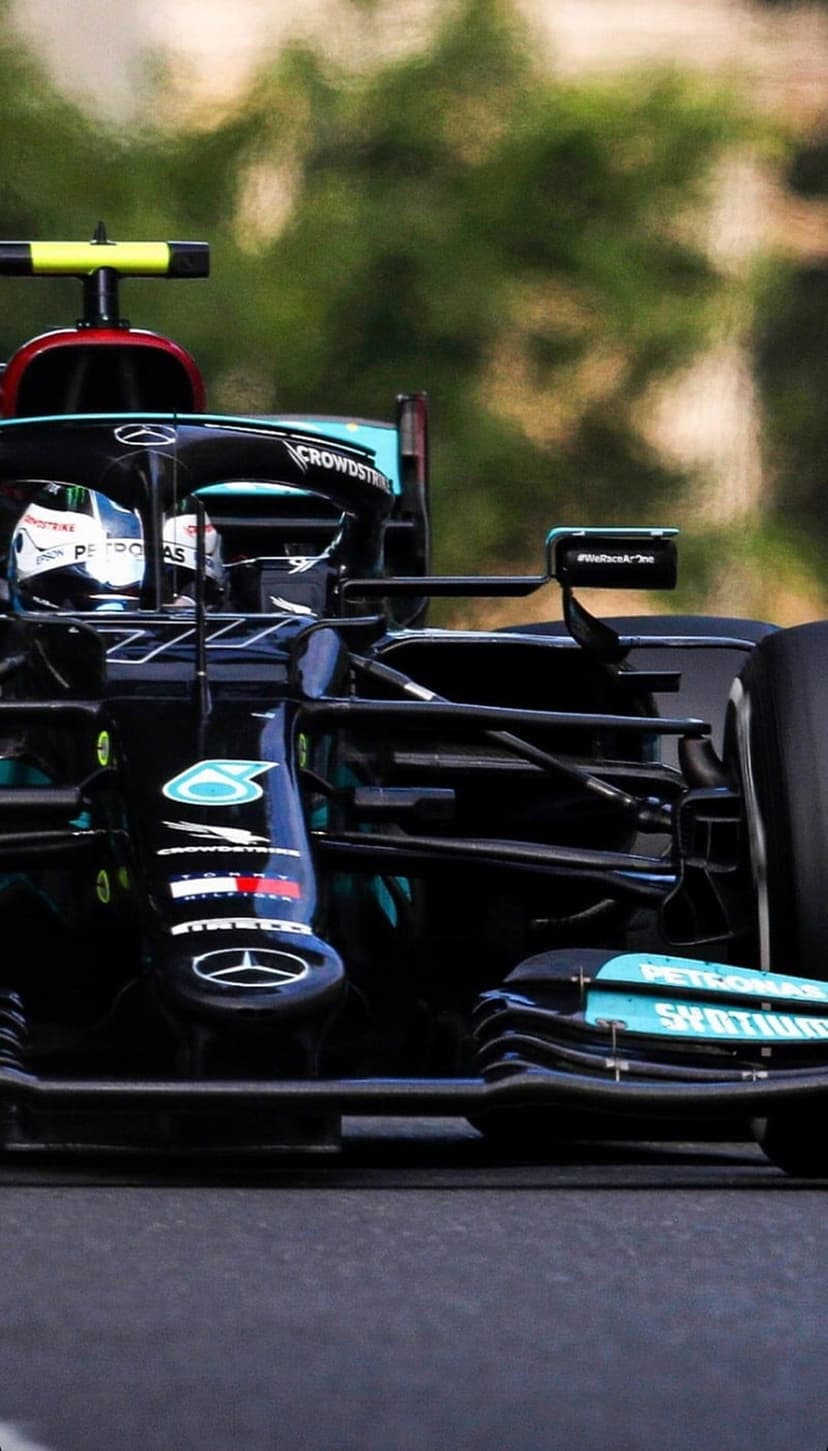 Mercedes Formula 1 car with Petronas branding races on a track against a backdrop of blurred green trees.