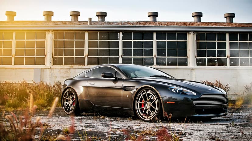 Dark gray Aston Martin supercar parked in front of an industrial building during a golden hour sunset.