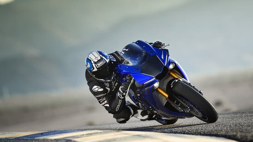 Blue Yamaha sportbike leans deep into a sharp turn on a racetrack with a rider in professional racing gear.