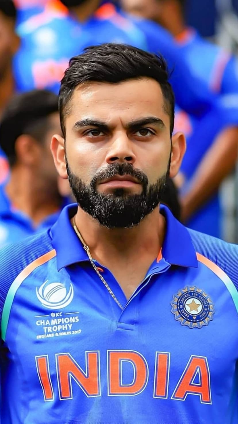 Virat Kohli in a blue India cricket jersey with an intense expression and beard against a blurred background.
