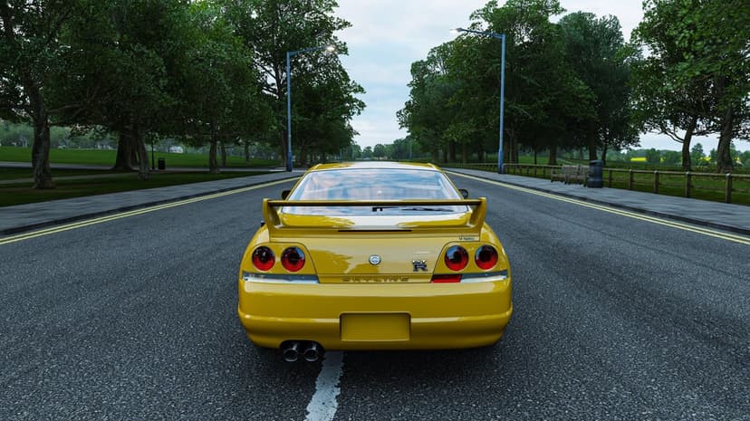 Rear view of a yellow Nissan Skyline GT-R R33 V-Spec on a two-lane road lined with green trees and lampposts.