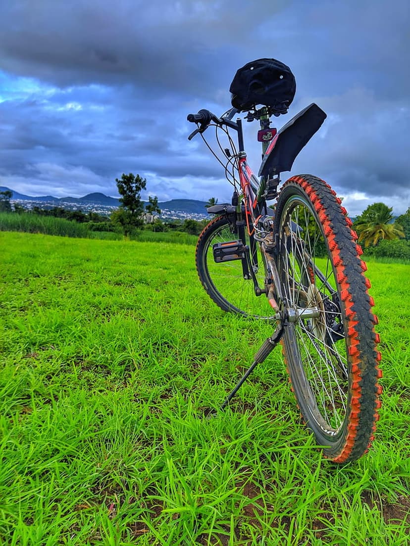 Mountain bike with orange tires parked on a lush green hill under a dark, dramatic, and cloudy storm sky.