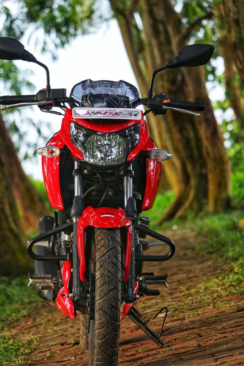 Red Apache motorcycle front view parked on a wooden walkway within a dense, green forest setting with soft light