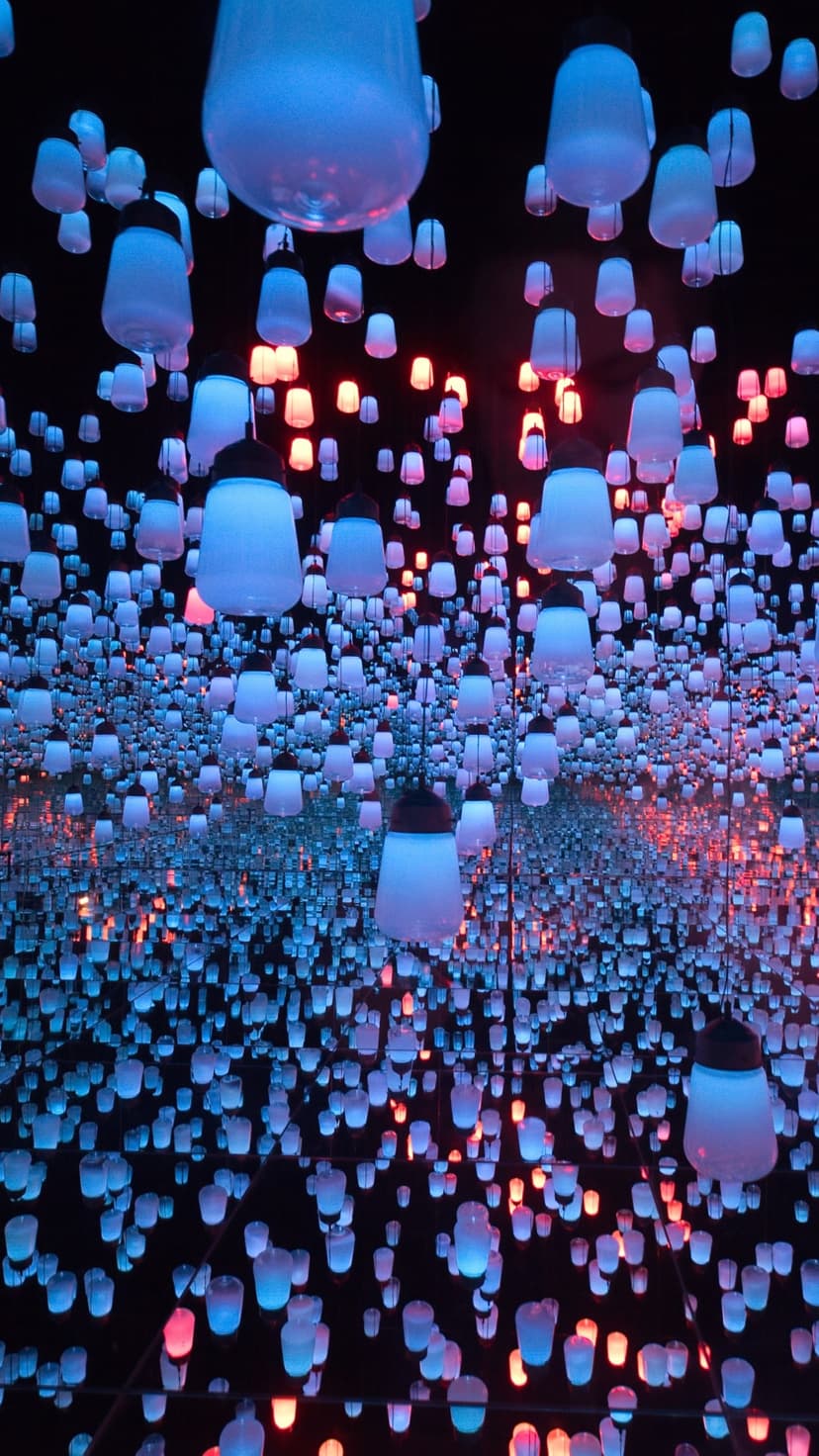 Glowing blue and red lanterns hang in a mirrored room creating a sense of infinite depth and light.