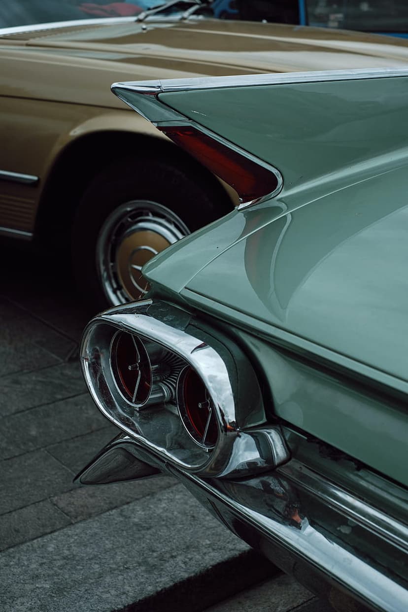 Teal Cadillac rear fins with red bullet taillights and polished chrome bumpers on a vintage mobile background.