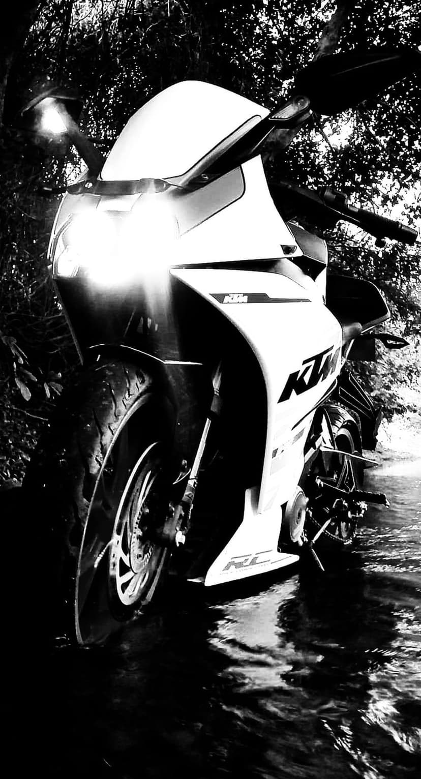 KTM motorcycle with glowing headlights reflected in dark water against a background of shadowy foliage.