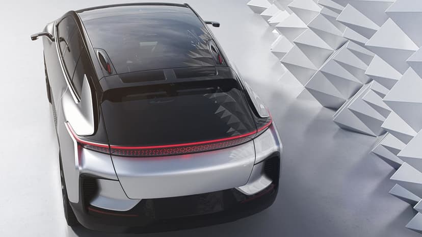 Silver electric car with a continuous red taillight bar parked next to geometric white wall structures.