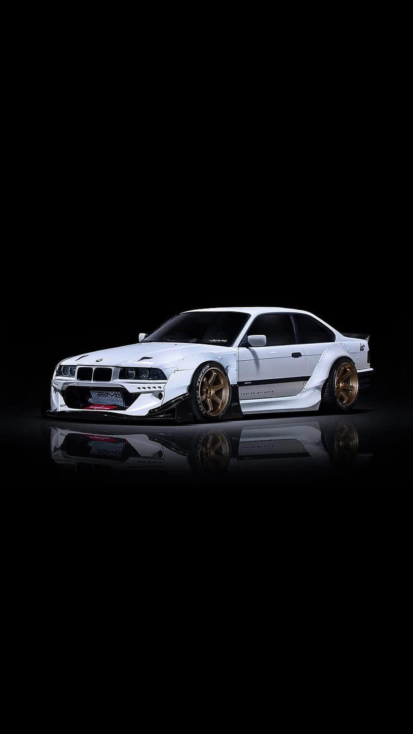 White BMW M3 E36 drift car with a widebody kit and bronze wheels parked against a solid black background.