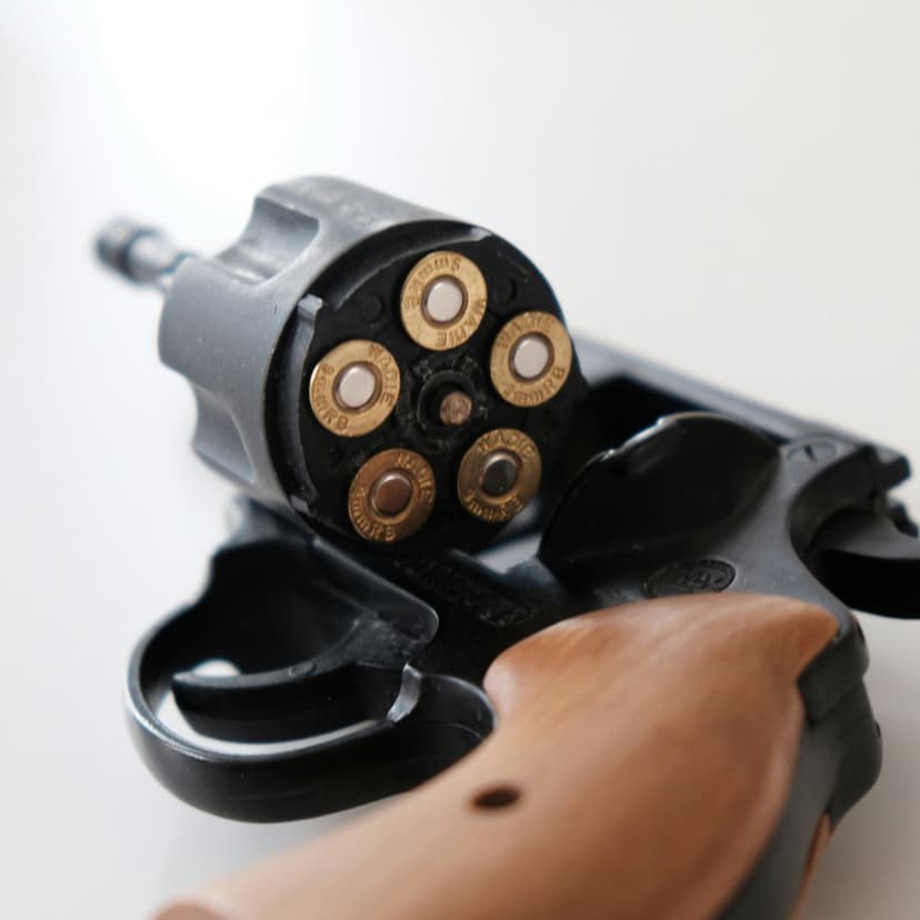 Revolver cylinder holding five brass cartridges against dark metal with a polished wooden grip visible on the side.