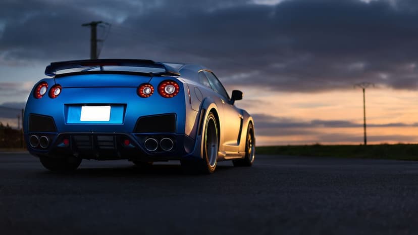 Blue Nissan GT-R widebody parked on a dark road at sunset beneath a dramatic, cloudy twilight sky.