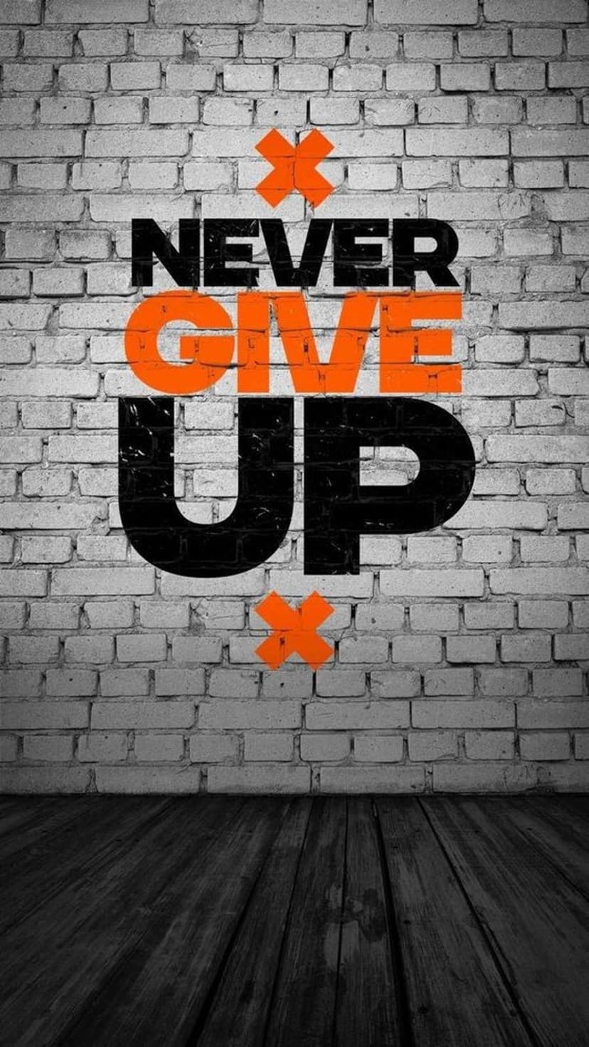 Bold Never Give Up quote on a weathered brick wall above a dark wooden floor with orange X accents throughout.