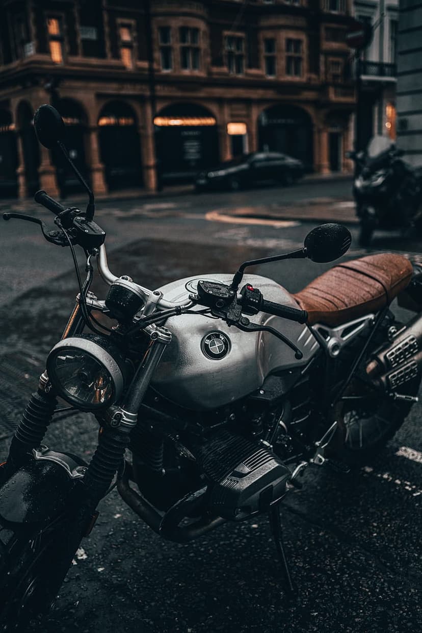 Silver vintage BMW motorcycle with a brown leather seat parked on a wet asphalt city street during twilight.