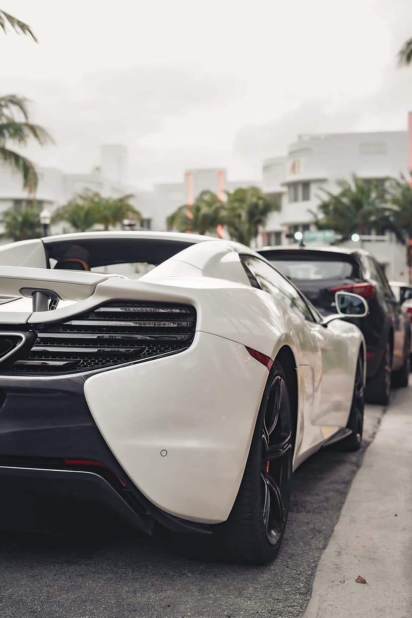 White McLaren rear view on a tropical city street lined with palm trees and modern buildings under soft light.