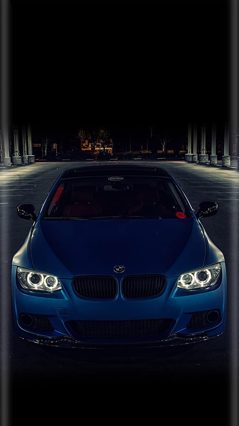 BMW coupe front grille and glowing blue halo headlights captured from a low angle against a dark night sky.