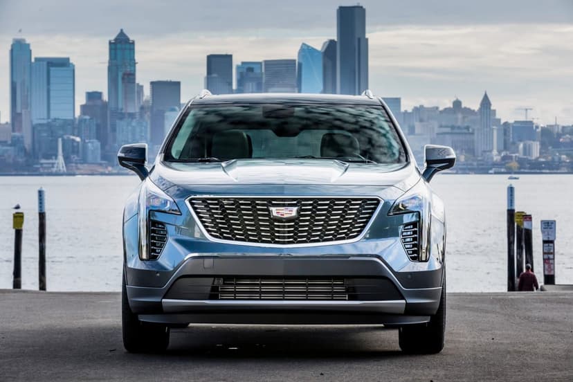 Silver Cadillac SUV front view with a detailed grille against the Seattle city skyline at a waterfront.