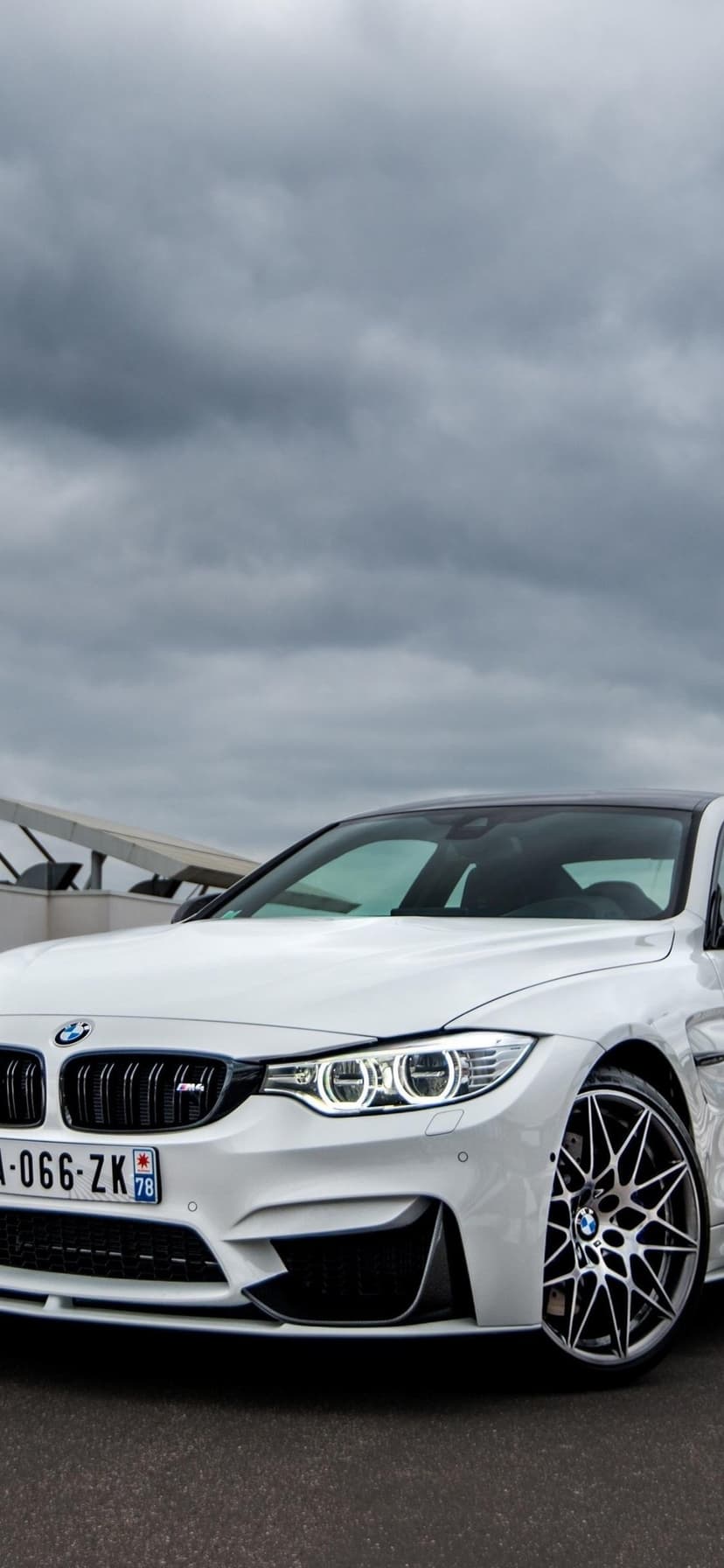 White BMW M4 sports car with glowing LED headlights and multi-spoke wheels under a dark cloudy sky.