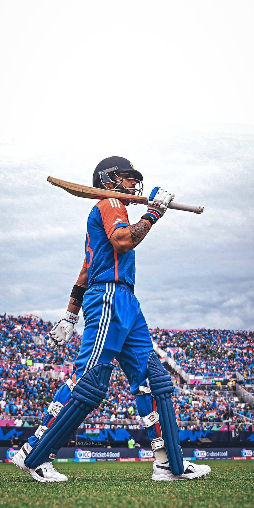 Virat Kohli walks off a cricket field carrying a bat over his shoulder while wearing a blue jersey and helmet.