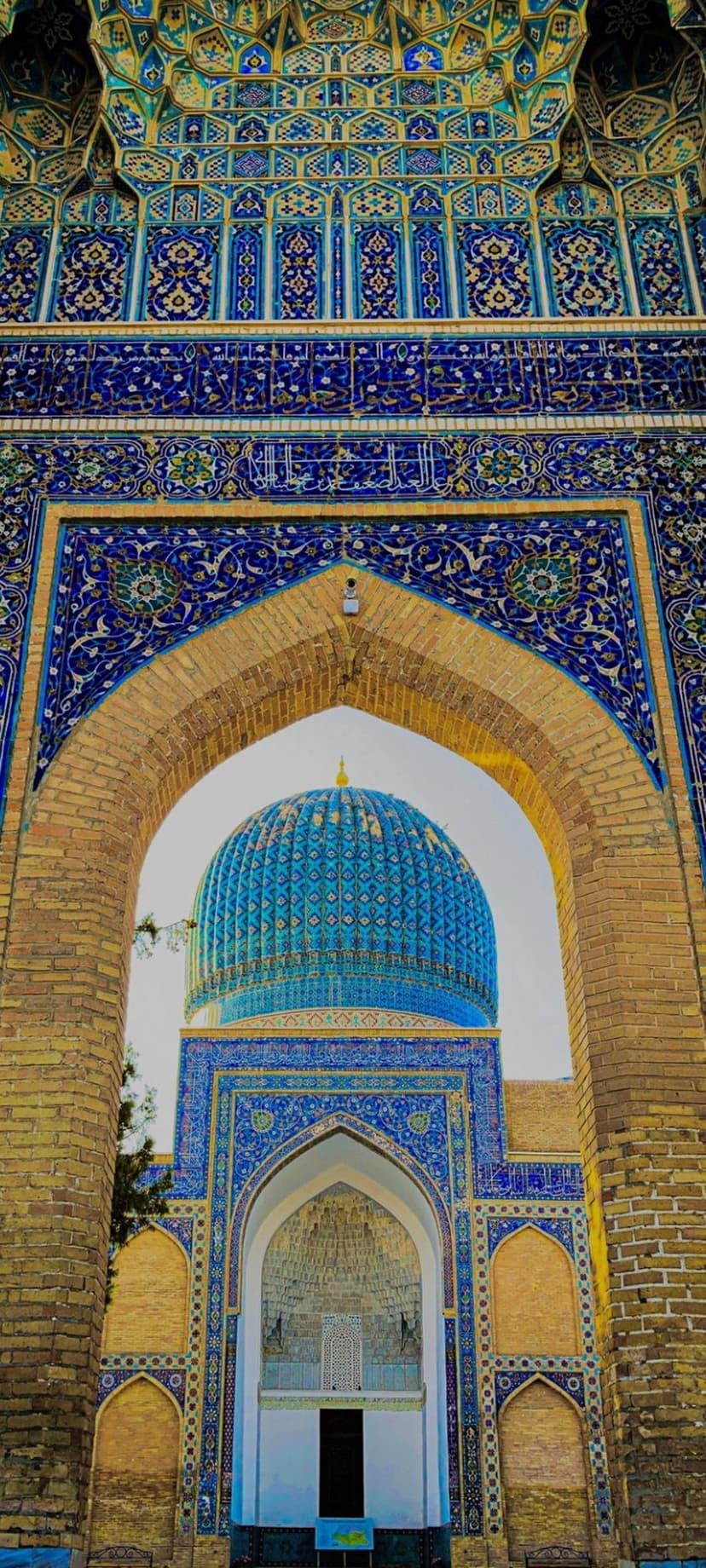 Blue tiled dome and arched entrance of a mosque featuring intricate geometric mosaics and Arabic calligraphy.