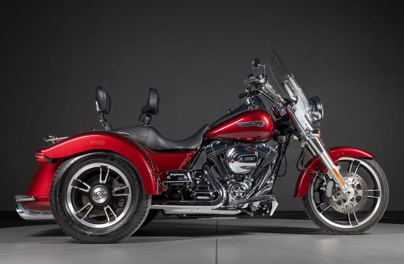 Side profile of a red Harley-Davidson trike with chrome engine details against a dark studio background.