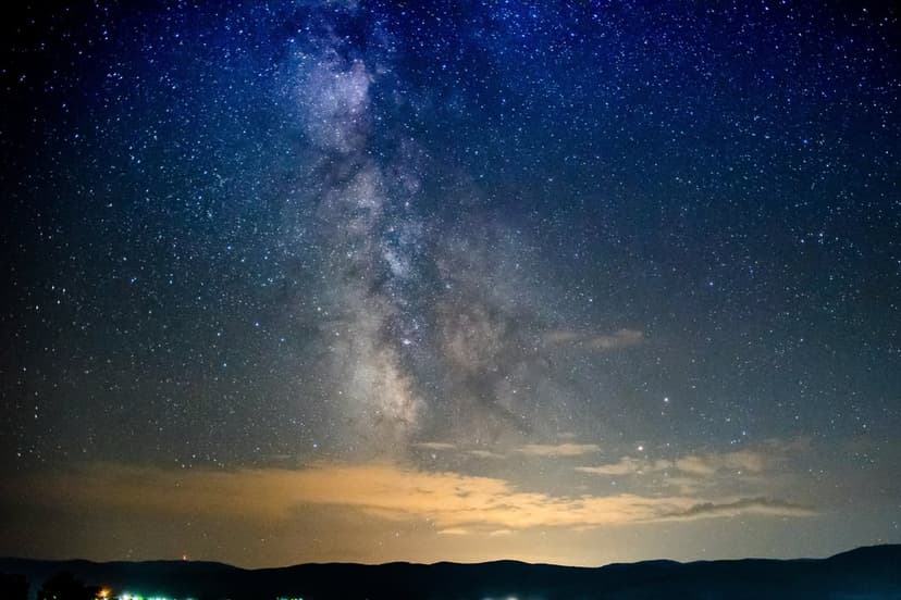 Milky Way galaxy with a dense band of stars and nebulae stretching vertically over a dark silhouetted horizon.